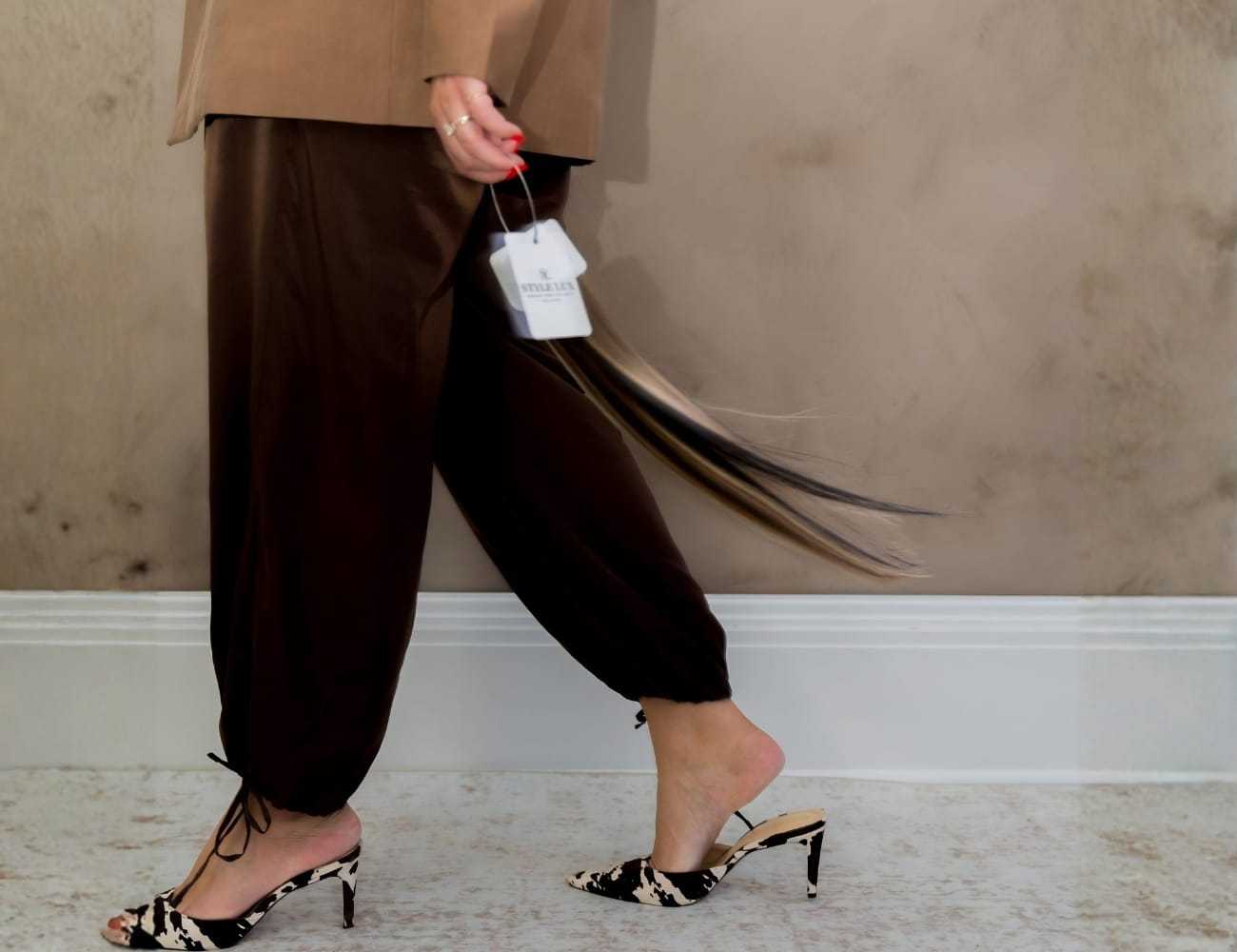 A person walking in stylish brown pants and heels, holding clothing tags.