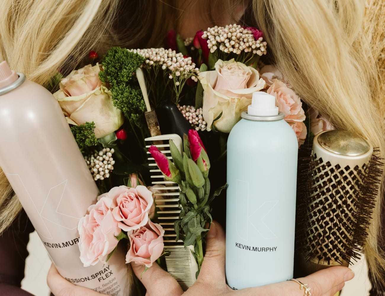 Hair products and flowers held by a person with long blonde hair.