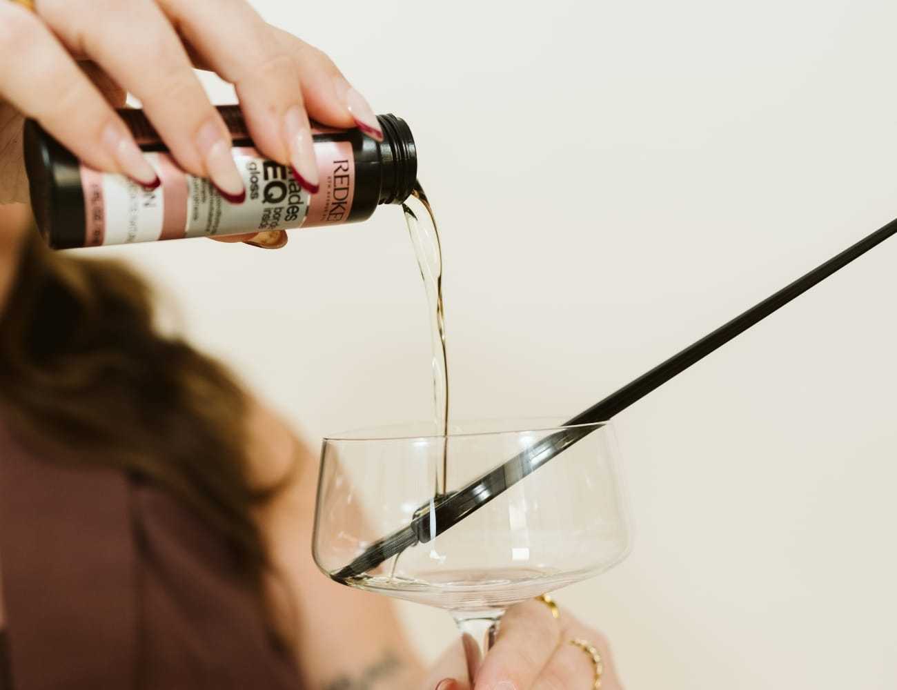 Pouring liquid from a bottle into a cocktail glass with a straw.