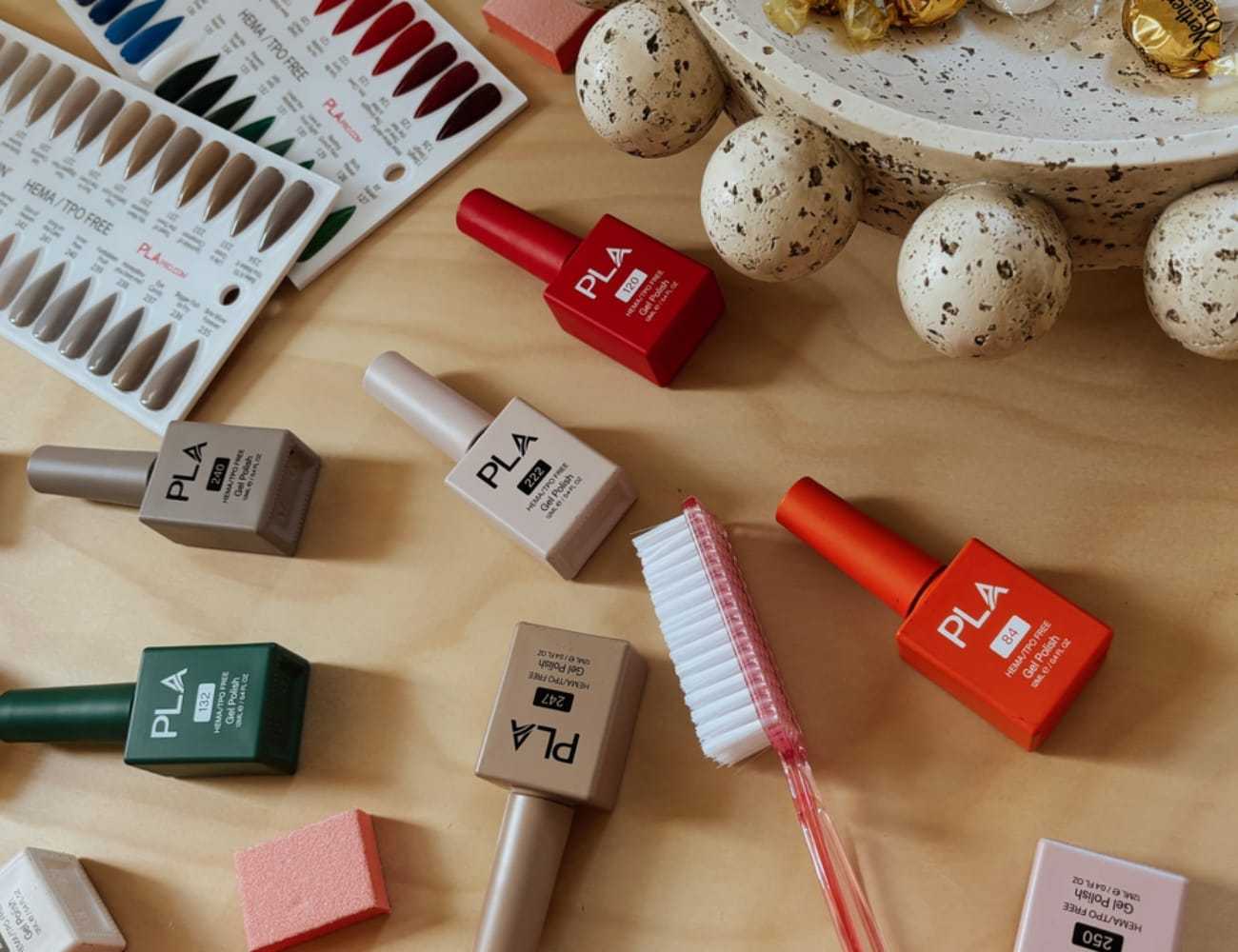 Nail polish bottles, a toothbrush, and sample palettes on a wooden surface with a bowl of candies.